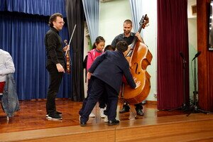 School children touching the body of a double bass to feel the vibrations of the resonance.